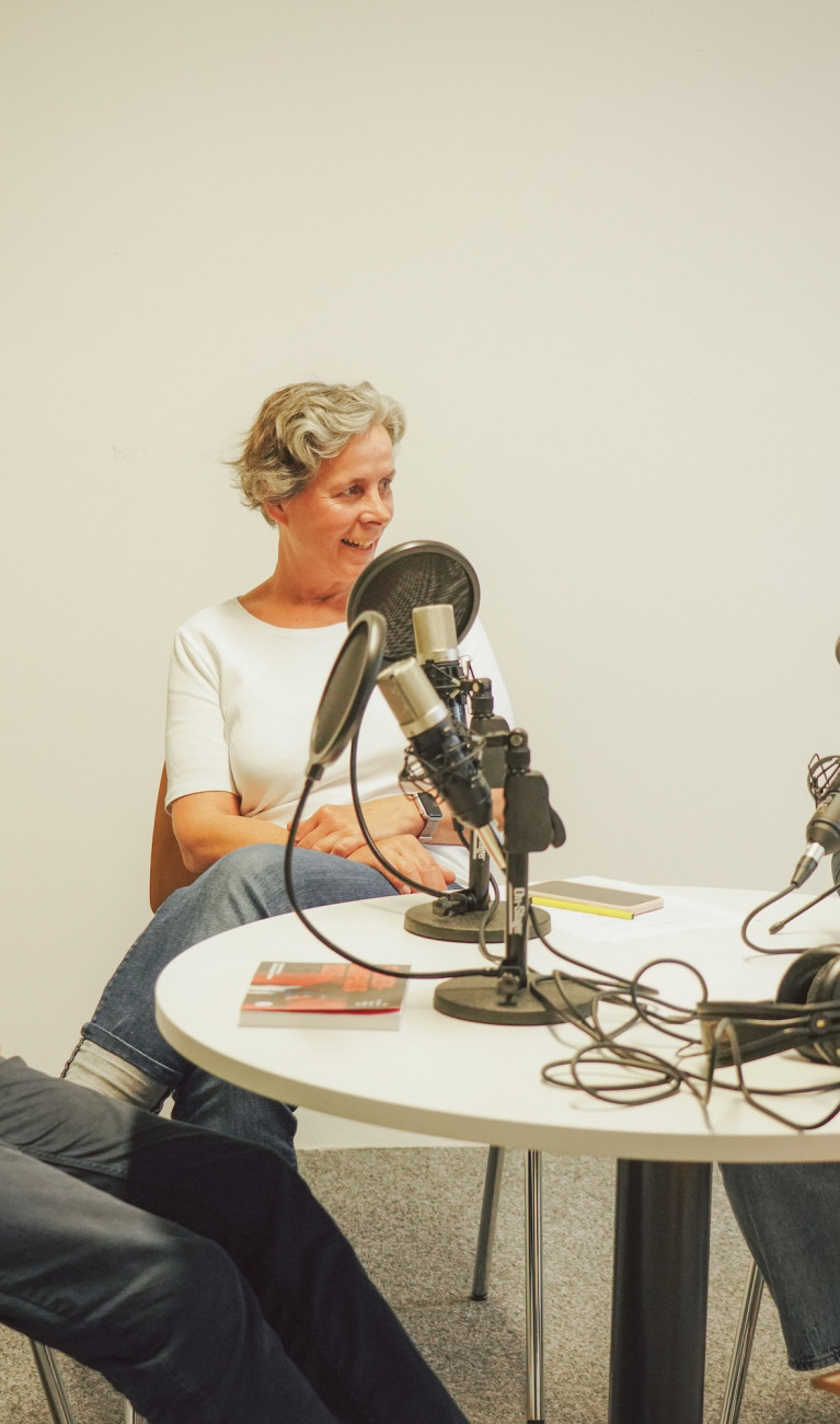 Drei Personen sitzen an einem runden Tisch bei einer Podcastaufnahme