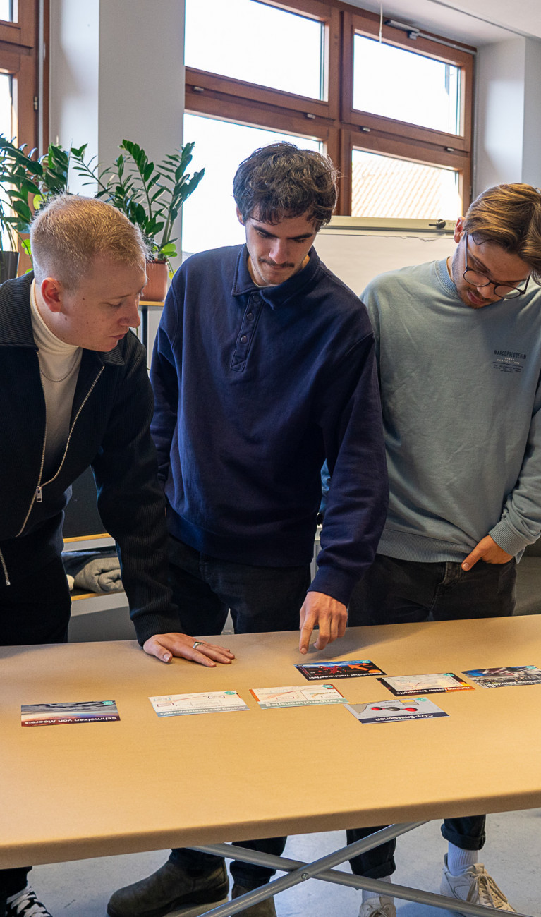 Personen stehen um einen Tisch herum und arbeiten interaktiv