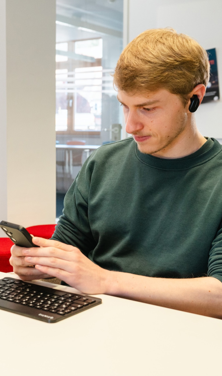 Ein junger Mann sitzt an einem Tisch und arbeitet am Laptop und Handy