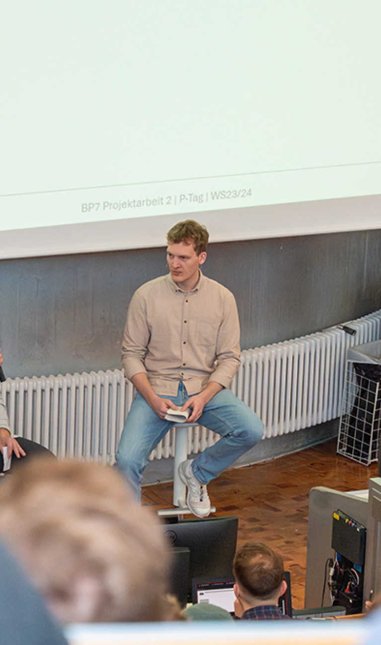 Drei Studenten sitzen im Vorlesungsraum vor der Leinwand und präsentieren