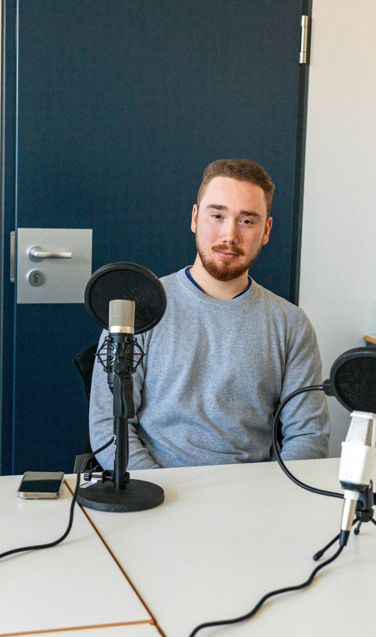 Drei Studierende sitzen mit Mikrofonen um einen Tisch