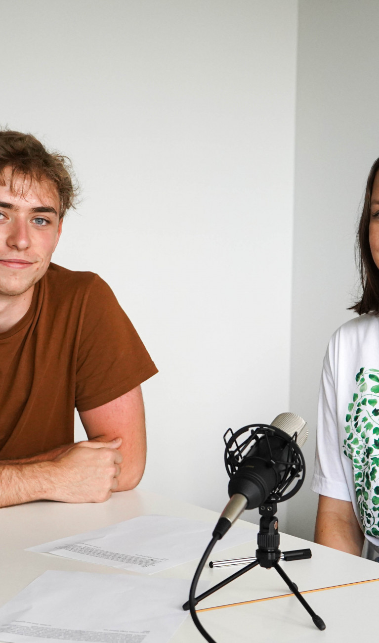 Ein Mann und eine Frau sitzend am Tisch bei einer Podcast-Aufnahme. 