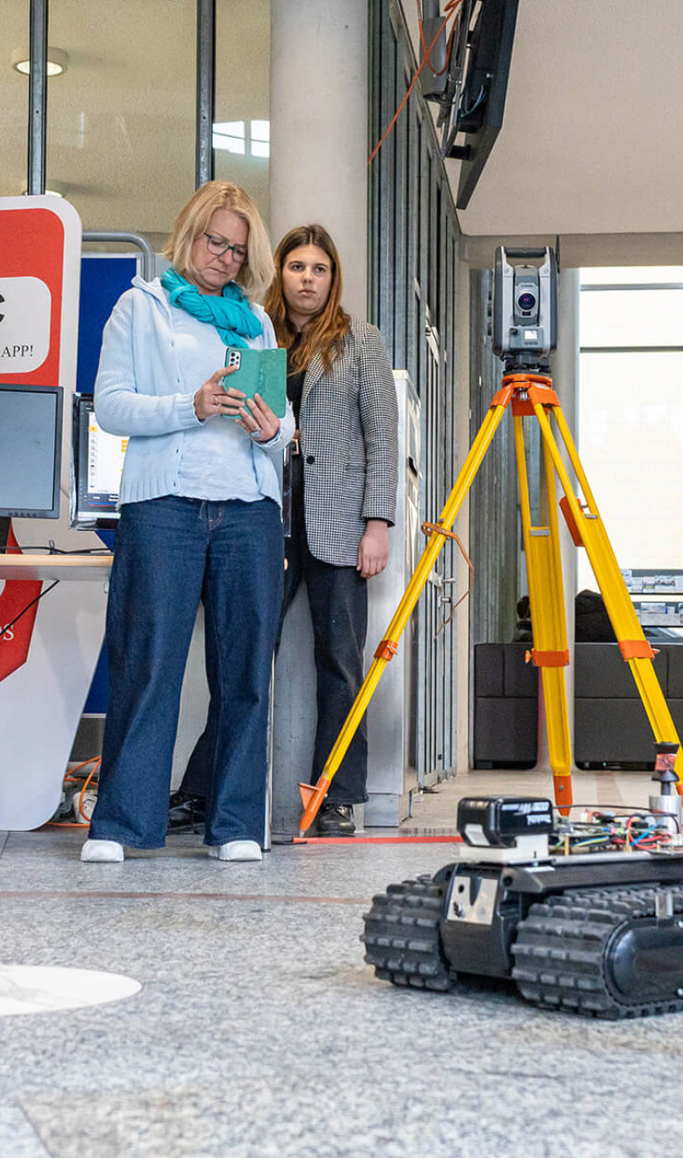 Eine Gruppe Studierender und Professor*innen steuert und filmt einen autonomen Roboter für die Baustelle