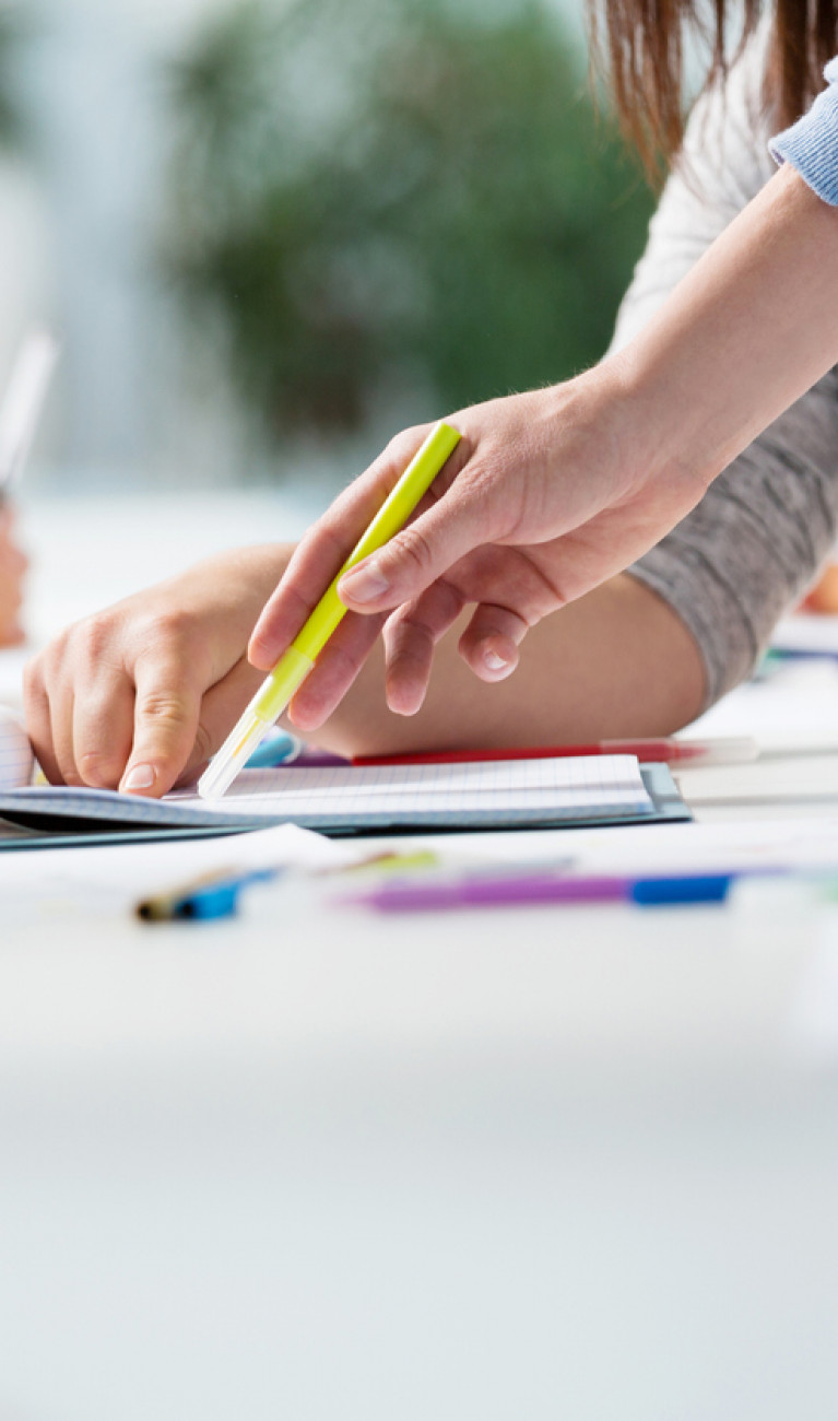 Schreibtisch mit Zetteln, bunten Siften und arbeitenden Personen