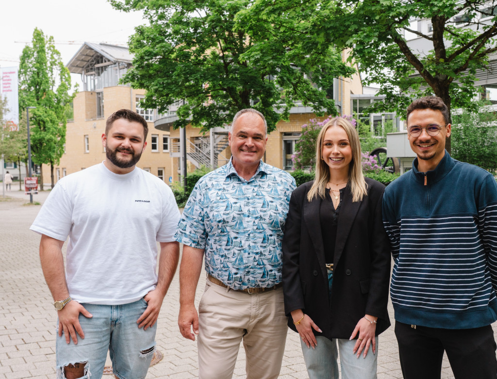 Drei Studierende stehen mit einem Professor auf dem Campus