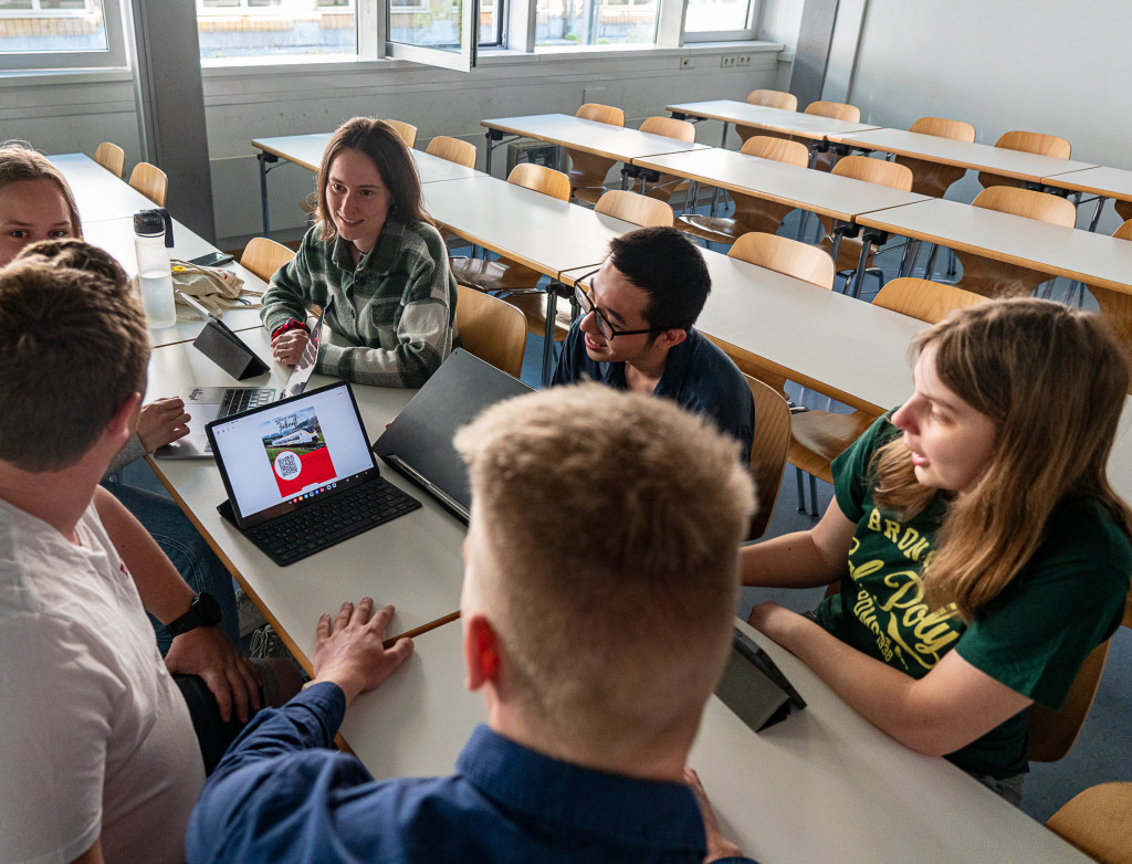 Sechs Studierende sitzen um einen Tisch mit geöffnetem Laptop