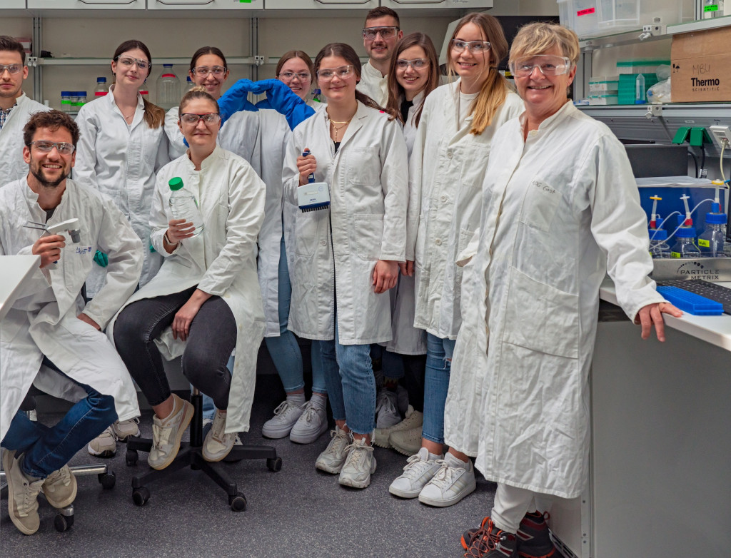 Gruppe von Menschen in Laborkitteln und mit Schutzbrillen