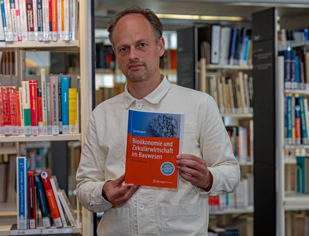 Mann steht in Bibliothek und hält Buch hoch