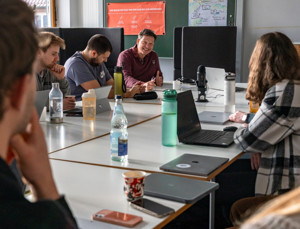 Studierende und ein Professor sitzen um einen großen Tisch und diskutieren