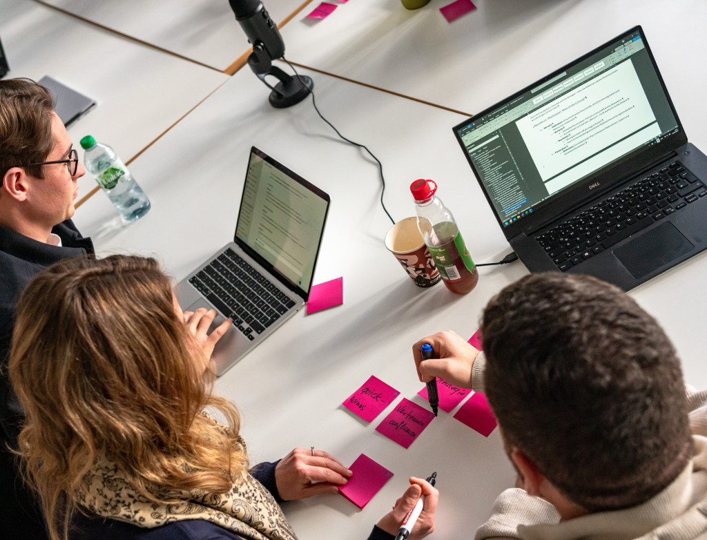 Studierende sitzen vor Laptops mit pinken Postits