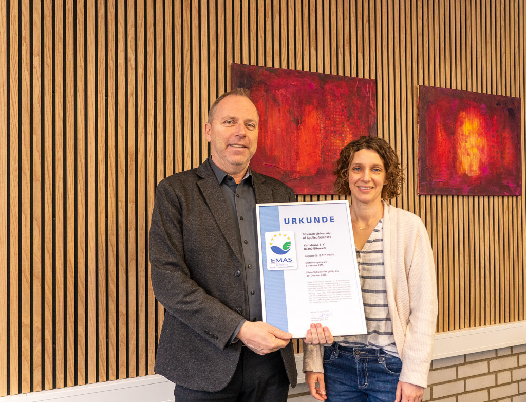 Ein Mann und eine Frau halte eine Urkunde von EMAS in die Kamera