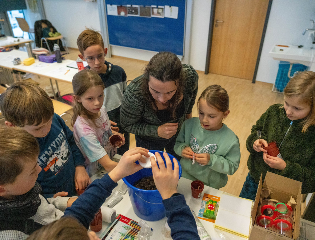 Kinder stehen mit Dozentin um Tisch und erforschen Boden