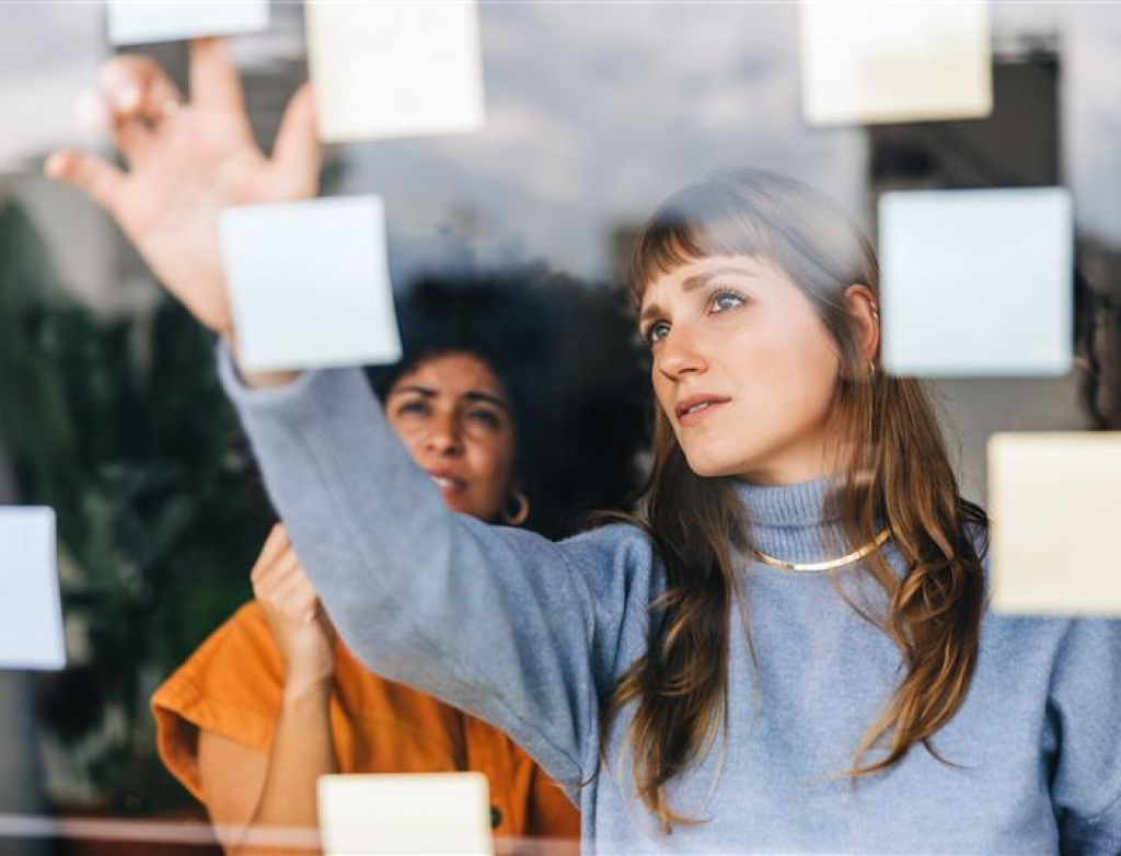 Zwei Frauen kleben Post it´s an eine Glasscheibe