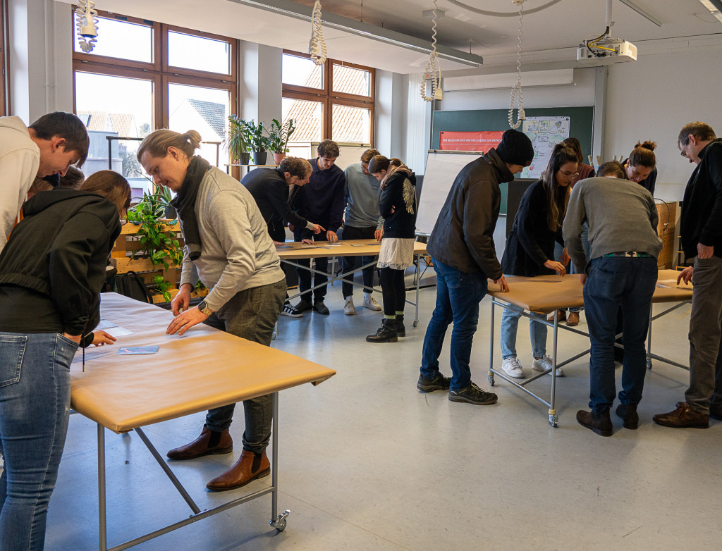 Personen stehen um drei Tische herum und arbeiten interaktiv