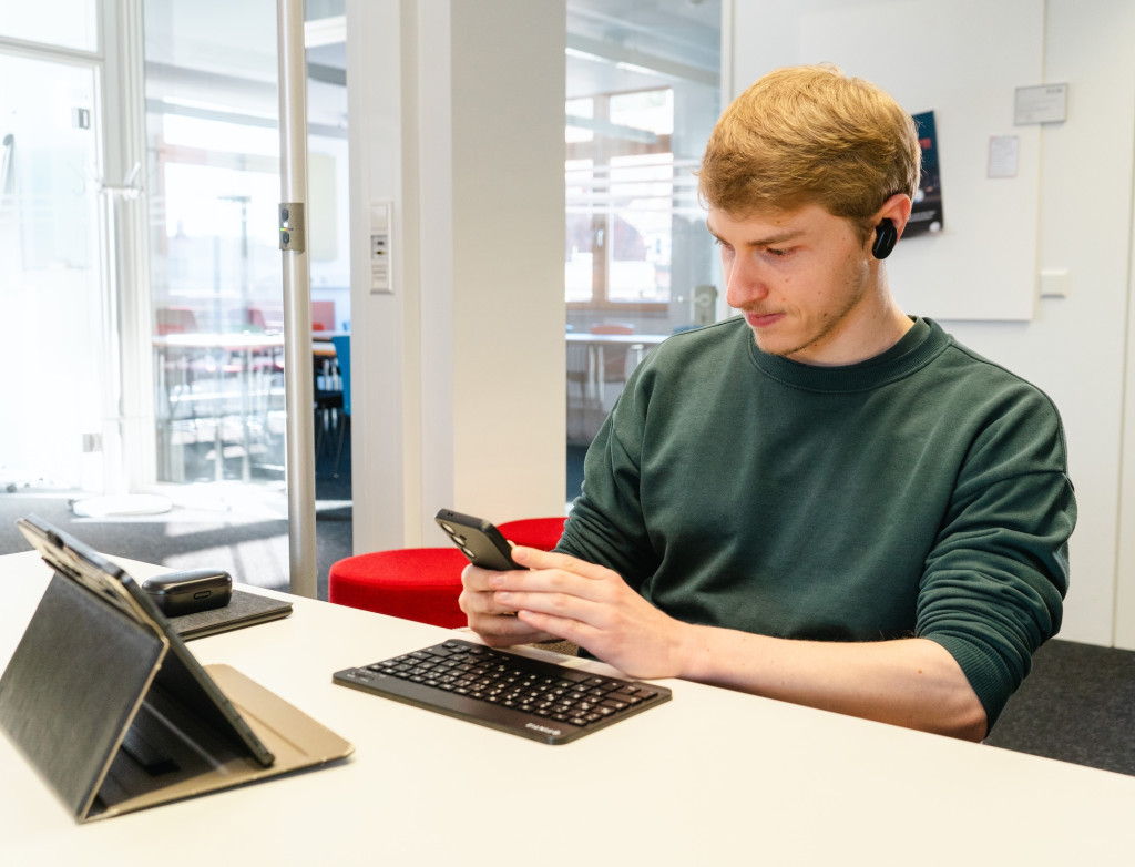 Ein junger Mann sitzt an einem Tisch und arbeitet am Laptop und Handy