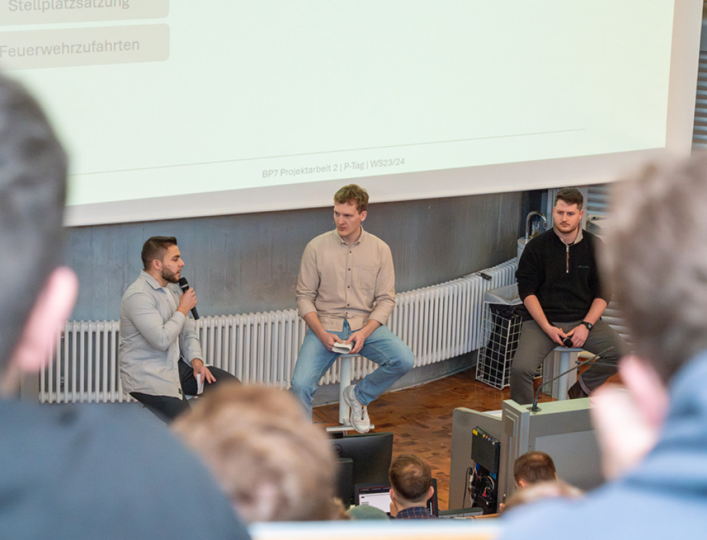 Drei Studenten sitzen im Vorlesungsraum vor der Leinwand und präsentieren