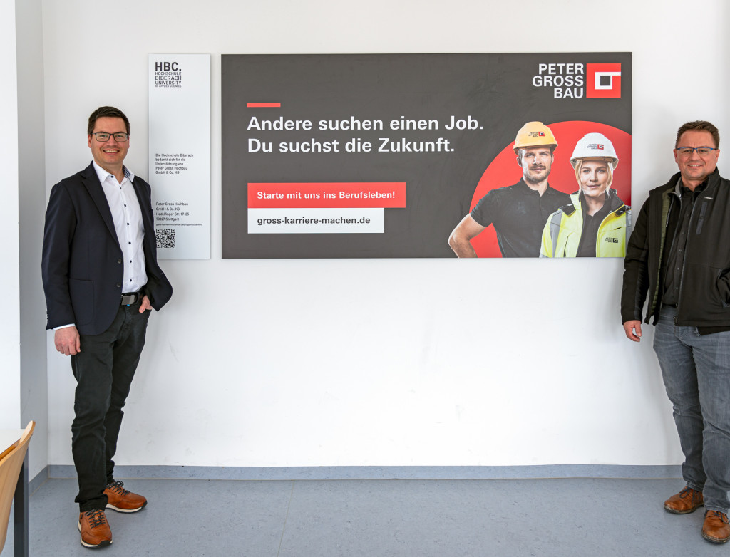Zwei Männer stehen links und rechts neben einem großen Banner von Peter Groß Bau