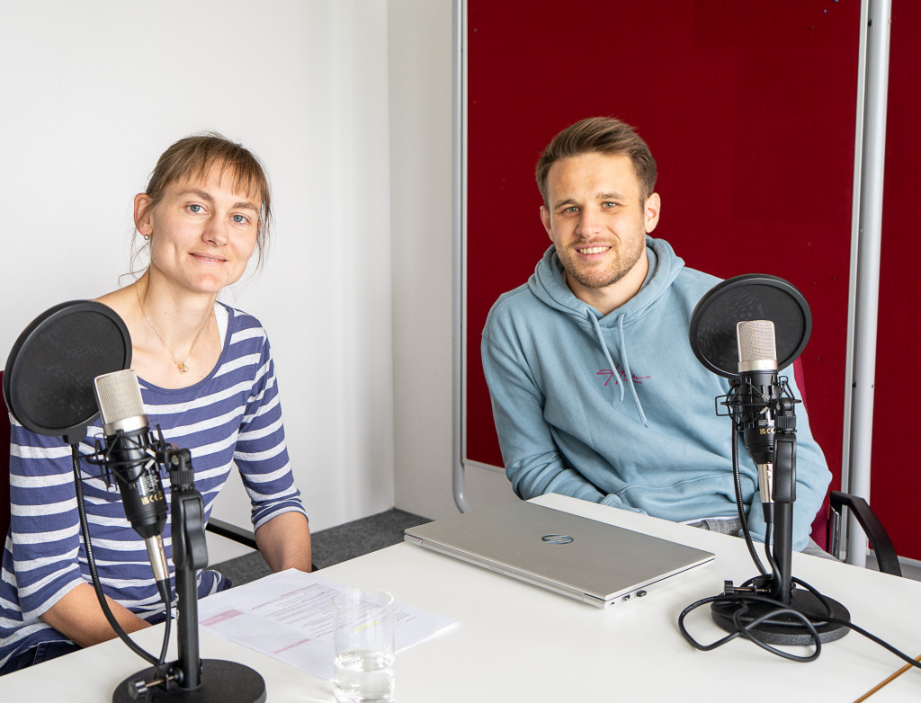Eine Frau und ein Mann sitzen an einem Tisch und nehmen einen Podcast auf