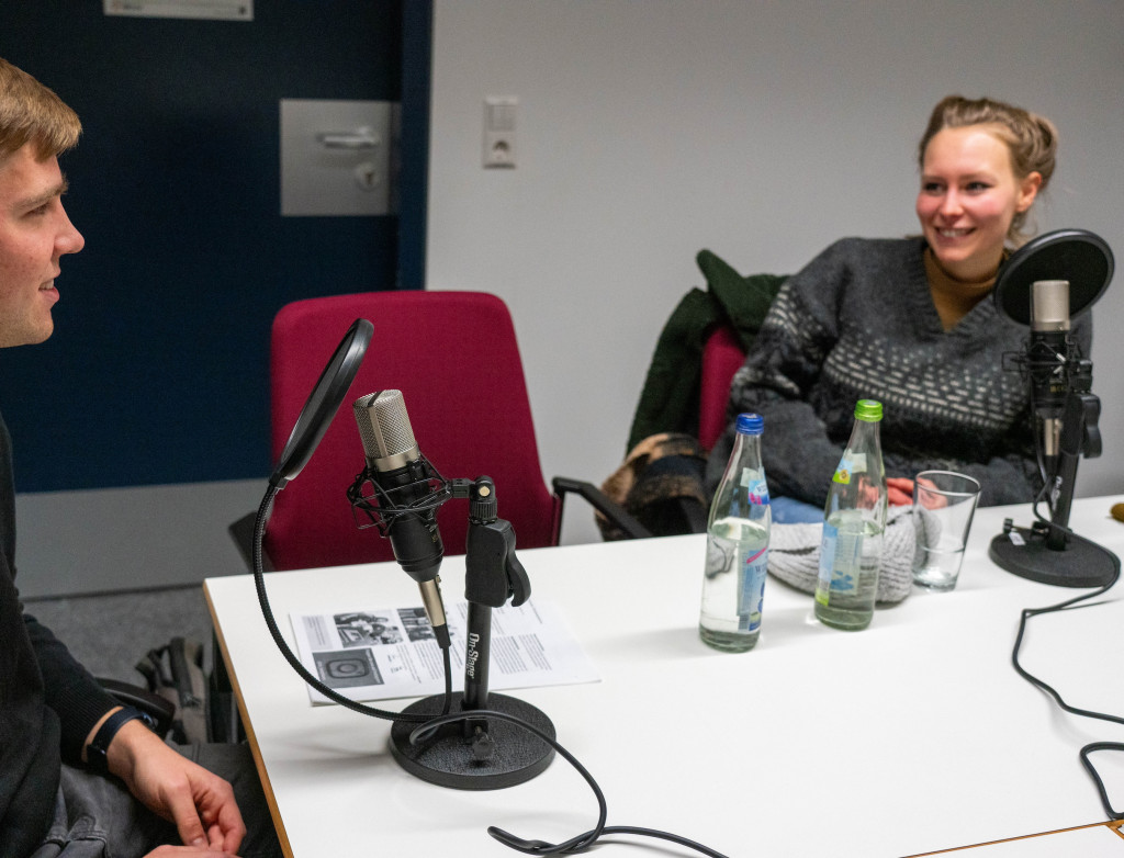 Ein Mann und eine Frau sitzen an einem Tisch bei Podcastaufnahme