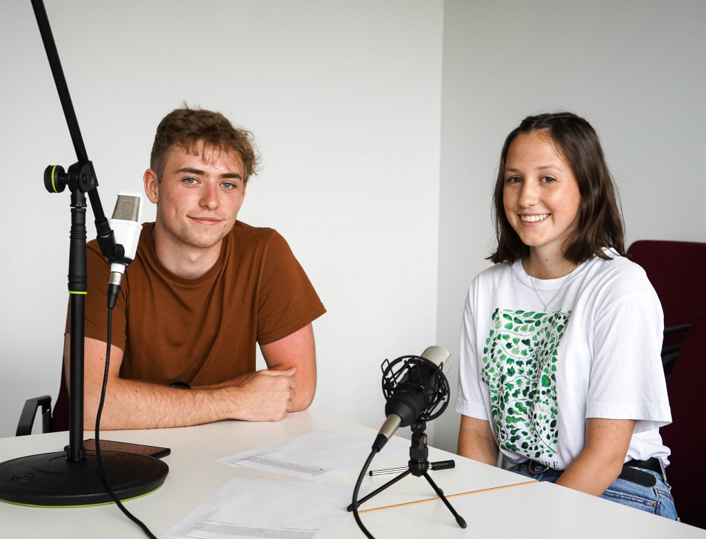 Ein Mann und eine Frau sitzend am Tisch bei einer Podcast-Aufnahme.