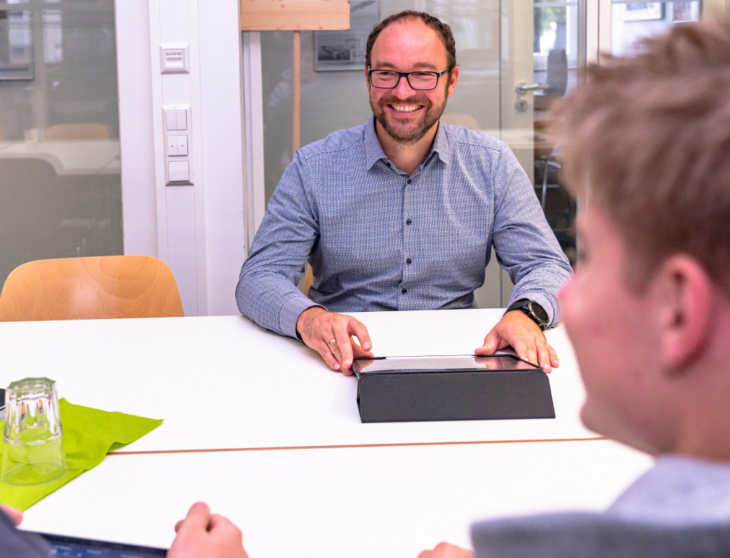 Mann sitzt mit zwei Studenten an einem Tisch