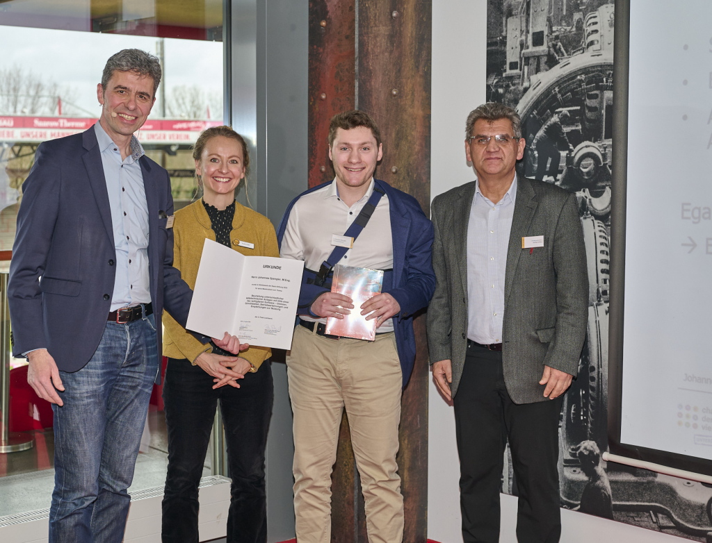 Vier Personen stehen lachend mit einer Urkunde