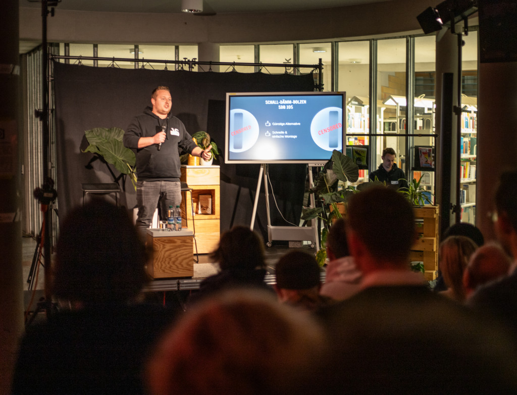 Mann steht in dunklem Raum auf einer Bühne