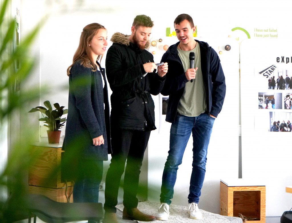 Drei Personen stehen bei einem Pitch auf einer Bühne