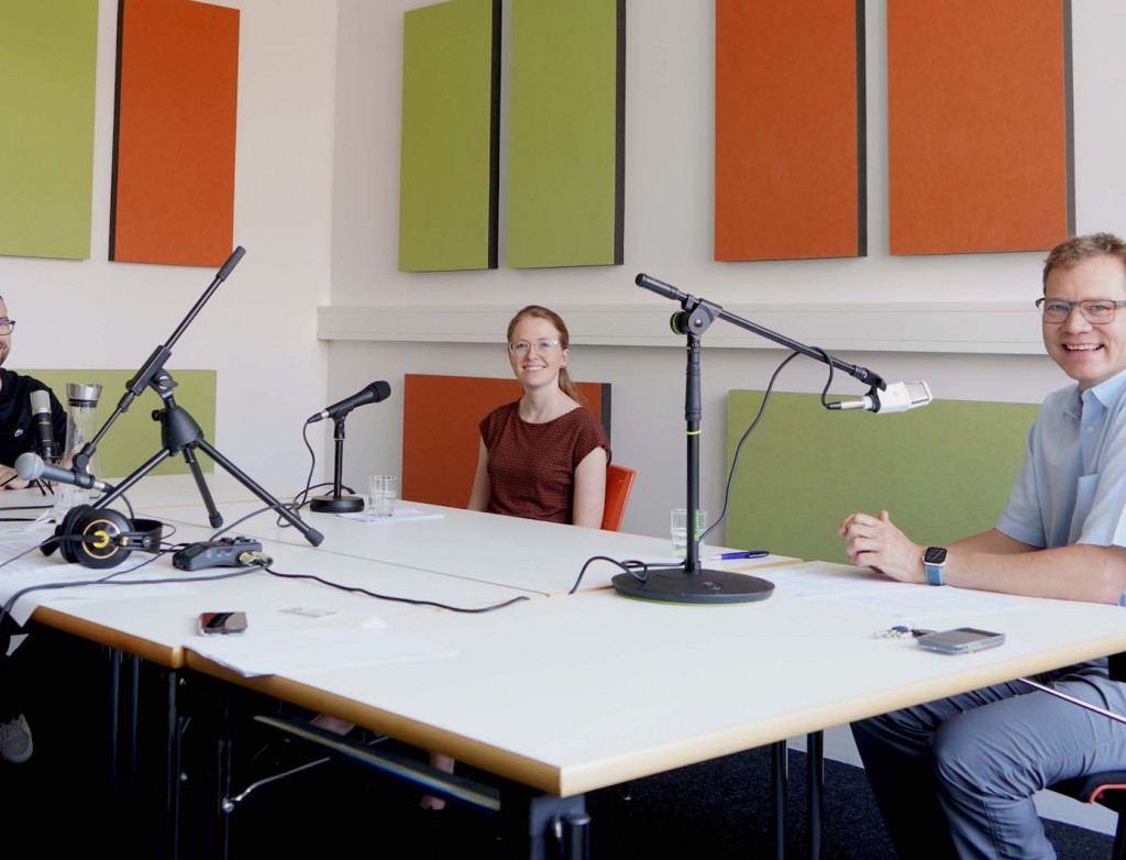 Drei Personen bei Podcastaufnahme an einem Tisch